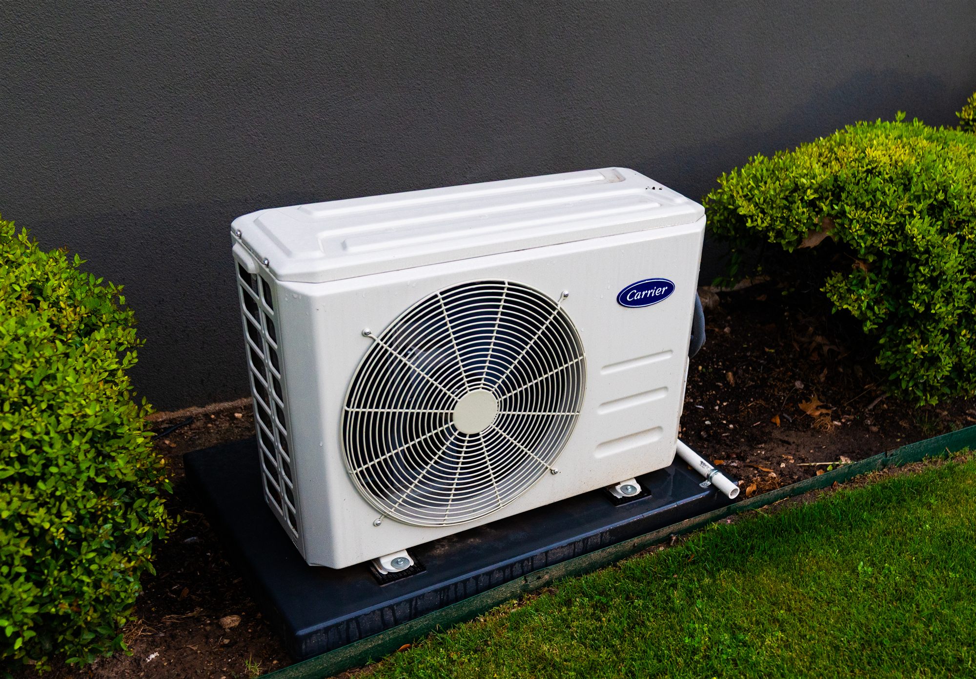 Outdoor mini-split condenser sitting on a pad beside a home